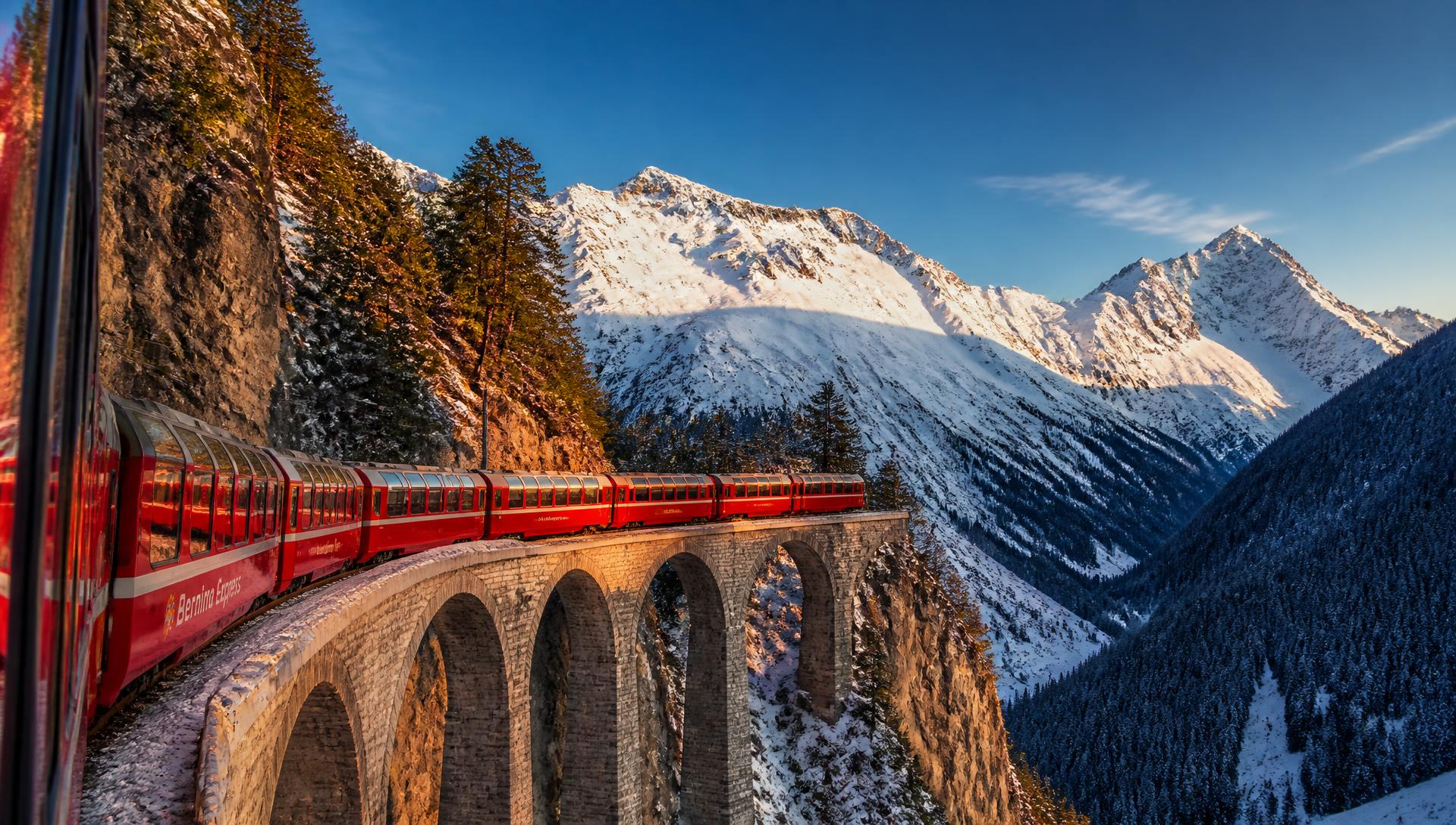 Panoramic train crossing an alpine viaduct in the Swiss Alps at golden hour